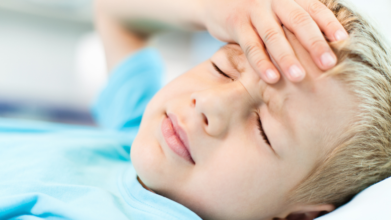 Young boy lying down holding his forehead with a headache