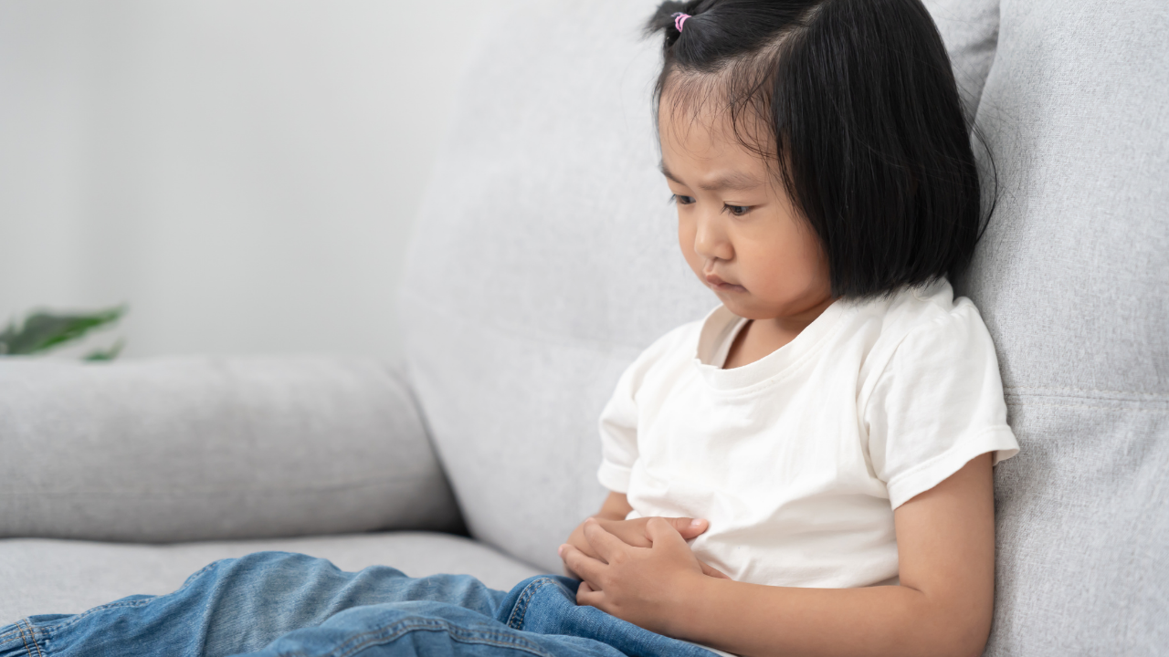 Young child sitting on a couch holding her stomach
