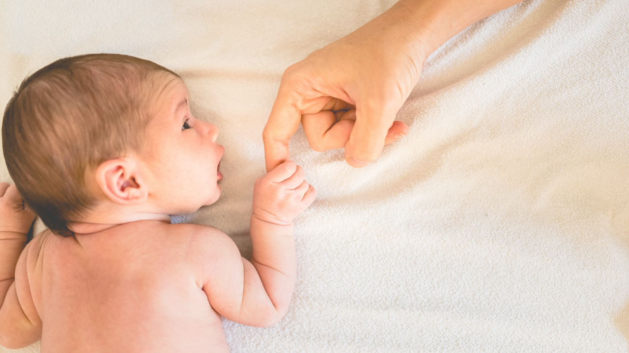 Newborn lying on a soft blanket holding a parent’s finger