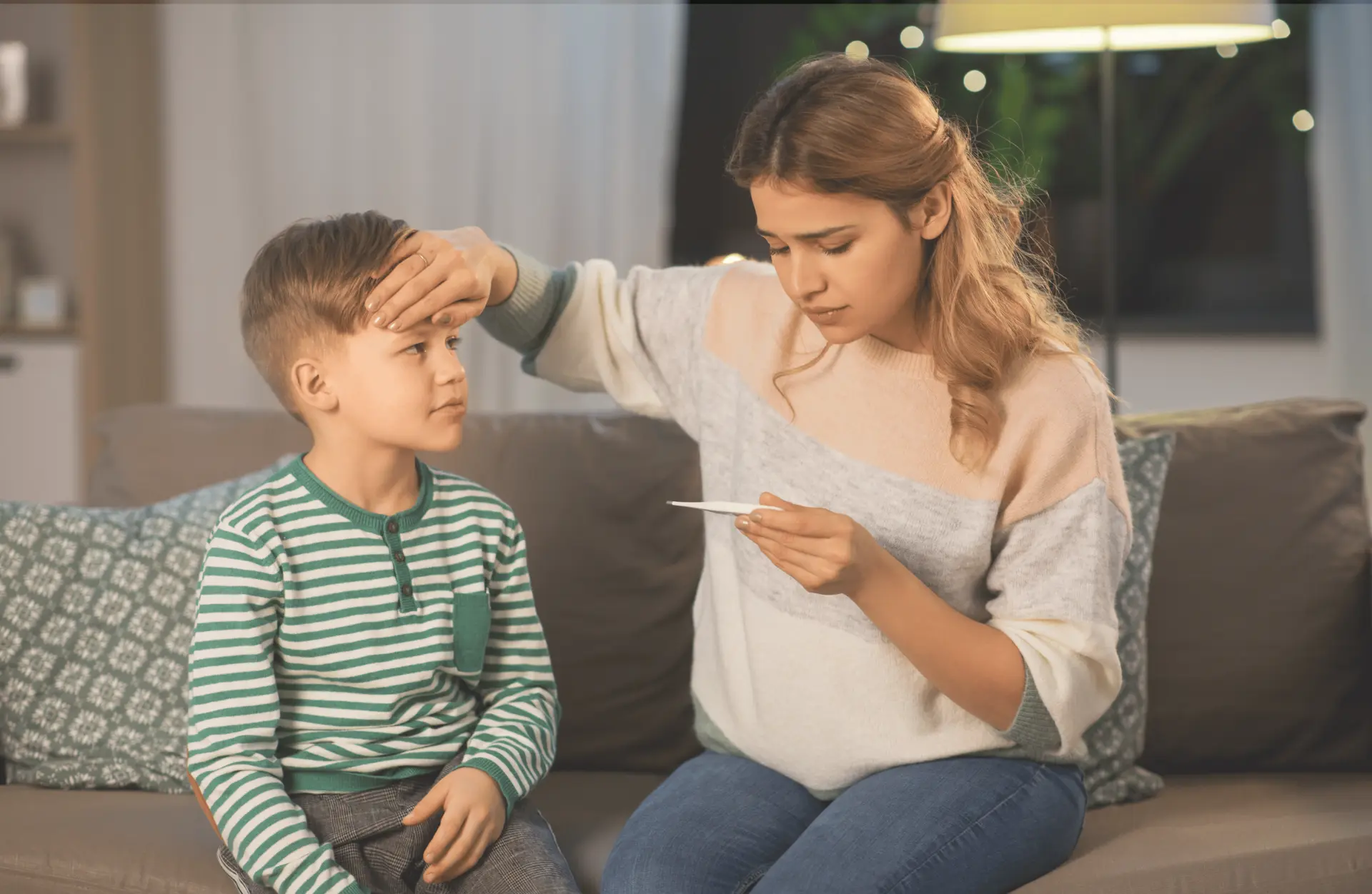 Mother checking child’s forehead with thermometer during a sick visit concern